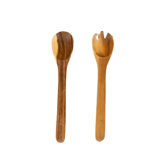 Two sustainably sourced utensils by LIKHA on a white background: the Acacia Essential Serving Set includes a wooden spoon on the left and a Fair Trade, two-pronged spork on the right.