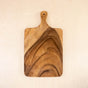 The LIKHA Acacia Cutting Board - Rectangle with handle is handcrafted from acacia wood, featuring rounded edges and unique natural grain patterns—a sustainable kitchenware piece displayed on a light wooden surface.