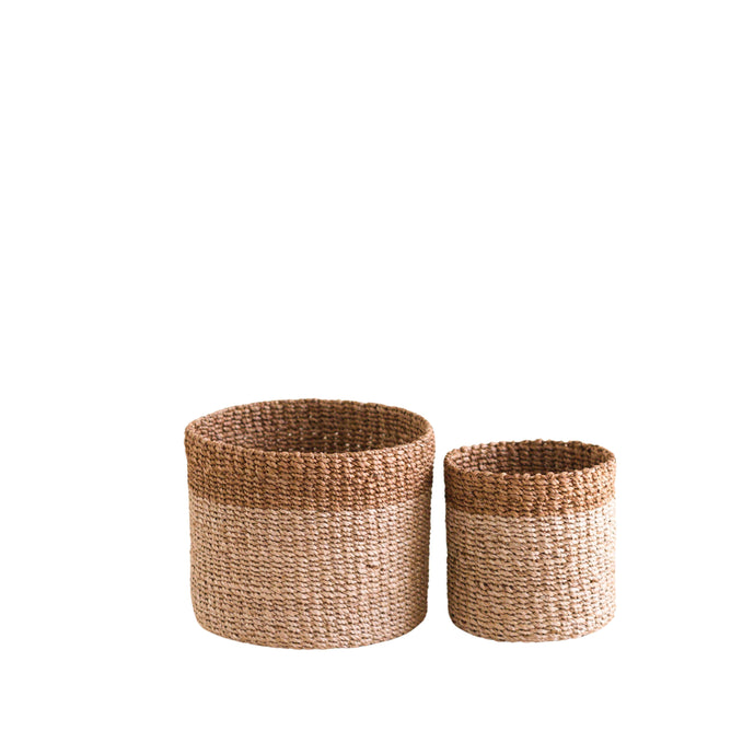The LIKHA Abaca Cylinder Tabletop Basket, a nested set of 2, features handcrafted natural brown Manila hemp in minimalist round designs. The two baskets are displayed side by side on a white background.