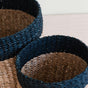 The LIKHA Abaca Cylinder Tabletop Baskets, a nested set of 2 handwoven from natural fibers, each featuring a brown base and dark blue rim, are displayed together on a light-colored surface.