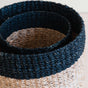 Close-up of two nested LIKHA Abaca Cylinder Tabletop Baskets, featuring natural beige and dark navy blue bands in a textured, hand-braided design. This Fair Trade Federation certified set blends style with ethical craftsmanship.