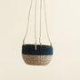 The LIKHA Abaca Round Hanging Planter features a handwoven beige bottom and dark blue top, suspended by four beige ropes against a plain, light background.