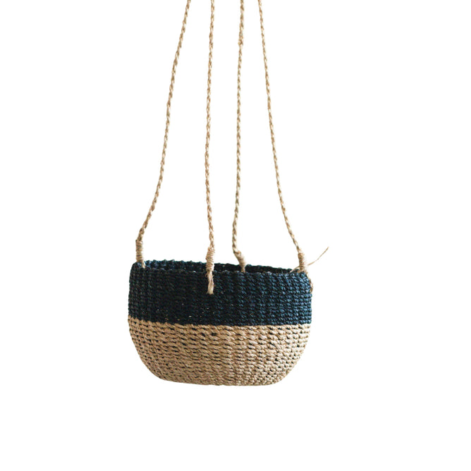 The LIKHA Abaca Round Hanging Planter features a handwoven two-tone design with natural beige on the bottom, dark blue on top, and four sturdy rope handles, shown suspended against a white background.