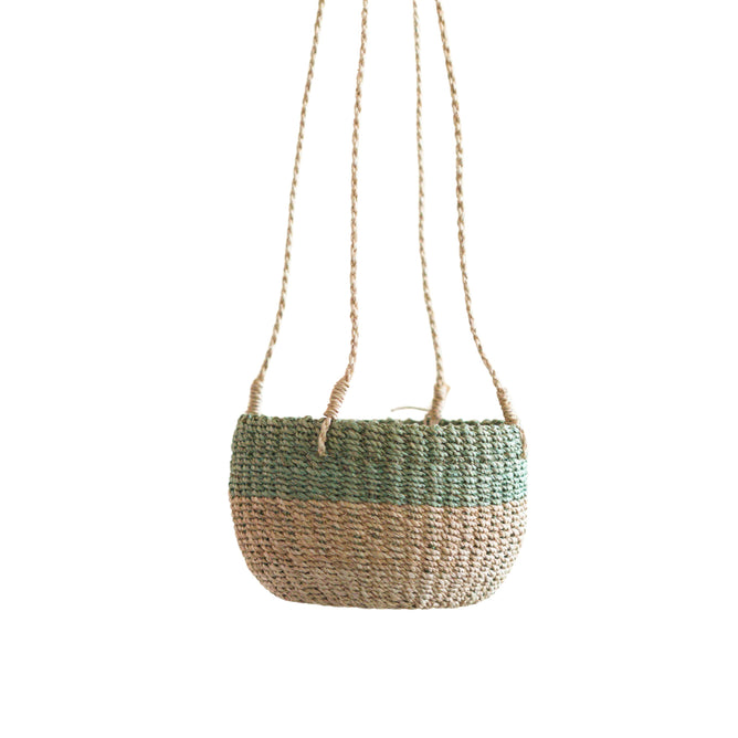 The LIKHA Abaca Round Hanging Planter features a green and natural two-tone woven abaca design with two long braided straps, displayed against a plain white background.