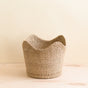 The LIKHA Abaca Scallop Basket, crafted from durable abaca fiber, rests on a light wooden surface. Its scalloped rim lends artisan charm, showcased against a plain beige background.
