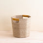The LIKHA Abaca Octagon Basket, handwoven in a natural hue with two yellow-wrapped handles, rests on a light wood surface against a pale background.