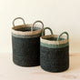 The LIKHA Abaca Cylinder Basket with handles is a nested set of 2 in different sizes, featuring dark green manila hemp bases and natural tops. Both baskets are displayed on a light wooden surface against a pale background.