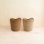 Two Abaca Small Scallop Baskets by LIKHA, ethically crafted from Manila hemp, sit side by side on a light wooden surface against a cream-colored background.