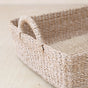 A close-up of the LIKHA Abaca Rectangle Tray with Handles highlights its sustainable craftsmanship, sturdy handle, and rectangular shape as it rests on a light wooden surface.