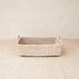 The LIKHA Abaca Rectangle Tray with Handles is handwoven from sustainable abaca, featuring two small handles, displayed on a light wooden surface against a beige background.