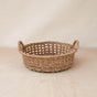 The LIKHA Abaca Round Tray Open Weave with Cutout Handles is a handwoven, shallow wicker tray made from 100% Manila hemp by Filipino artisans, displayed on a light wooden surface against a plain beige background.