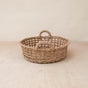 The LIKHA Abaca Round Tray Open Weave with Cutout Handles, an ethically made handwoven wicker basket, sits on a light wooden surface against a neutral beige background.