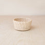 The LIKHA Abaca Mini Trinket Basket, handwoven from sustainable abaca fiber, sits round and neat on a light wooden surface against a plain beige background.
