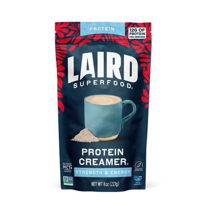 A bag of Laird Superfood Protein Superfood Creamer, featuring red leaf accents and 12g vegan protein per serving, is shown beside a blue coffee mug and powder. The creamer contains plant-based protein and superfood ingredients.