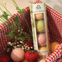 A Pacha Soap Co. Bath Bomb Set - Summer Garden, made with natural ingredients, sits in a red and white gingham basket among flowers, strawberries, and loose bath bombs. The packaging reads "Summer Garden Collection.