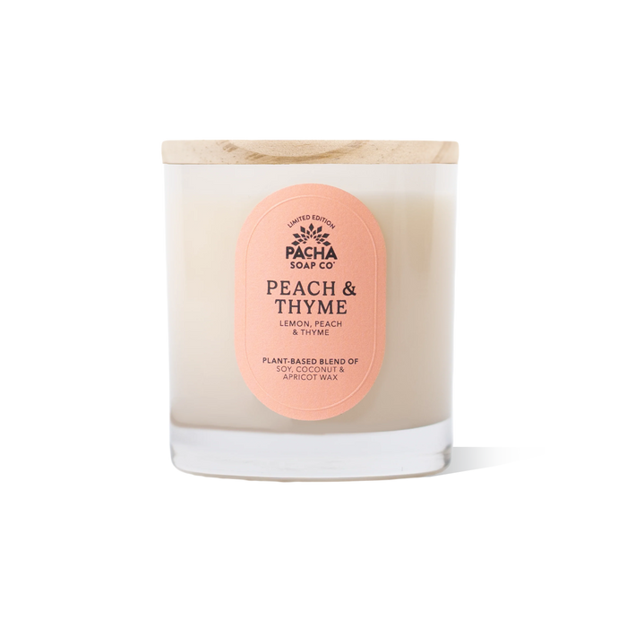 The Summer Signature Candle by Pacha Soap Co. is a white candle in a clear glass jar with a wooden lid, featuring a vegan, cruelty-free coconut and apricot wax blend for a clean burn. Label: Peach & Thyme.