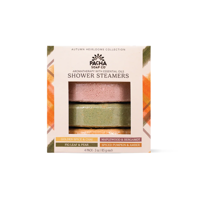 The Pacha Soap Co. Shower Steamer Set - Autumn Heirlooms Collection features a box containing four labeled autumn-inspired scents: Golden Spice & Chai, Maplewood & Bergamot, Fig Leaf & Pear, and Spiced Pumpkin & Amber. Through the package window, two round handcrafted shower steamers are visible.