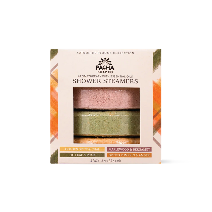 The Pacha Soap Co. Shower Steamer Set - Autumn Heirlooms Collection features a box containing four labeled autumn-inspired scents: Golden Spice & Chai, Maplewood & Bergamot, Fig Leaf & Pear, and Spiced Pumpkin & Amber. Through the package window, two round handcrafted shower steamers are visible.