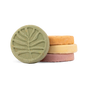 Four round shower steamers from the Pacha Soap Co. Autumn Heirlooms Collection, in green, orange, yellow, and pink, are stacked on a white background. The handcrafted green steamer at the front features an embossed leaf design and offers notes of autumn fragrance.