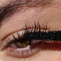 A close-up of a persons eye with long lashes coated in Ere Perez Lash to Lip Party-Proof Duo mascara, highlighting the detailed texture of the lashes and skin.