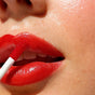Close-up of a person applying Ere Perez Lash to Lip Party-Proof Duo to their lips with a gloss applicator, showing smooth skin and part of the nose—ideal for achieving a flawless, party-ready makeup look.