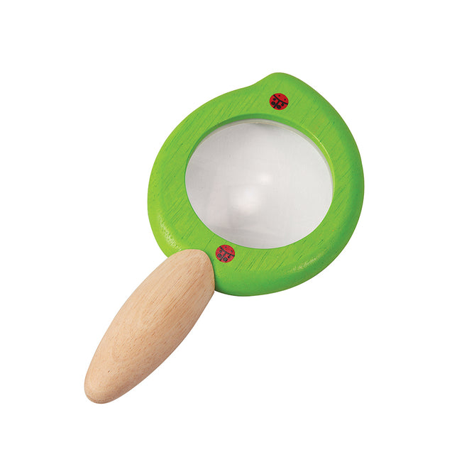 The PlanToys Leaf Magnifier features a green leaf-shaped design, wooden handle, and two red ladybug accents on the frame—ideal for toddlers’ outdoor discoveries. Shown against a white background.