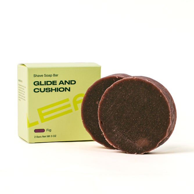 Two round, dark brown Leaf Shave Shave Soap bars sit before a light green Glide and Cushion, Fig box. Each bar weighs 3 oz, offering a creamy lather and a natural shaving experience.