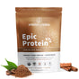 A prominently displayed brown and white Sprout Living Epic Protein package in Chocolate Maca flavor, labeled vegan protein powder, is surrounded by cacao powder, cinnamon sticks, and cacao beans with green leaves. It features a blend of organic plant protein enhanced with superfoods.