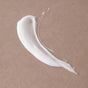 A smear of Pacha Soap Co. Body Lotion, enriched with hydrating coconut oil, is spread on a smooth, light brown surface.