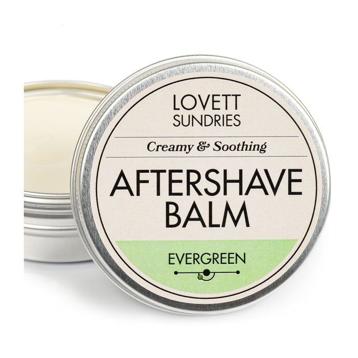 A round metal tin of Lovett Sundries Aftershave Balm features a Creamy & Soothing and Evergreen label with the lid slightly ajar, exposing the creamy balm ideal for soothing skin and preventing razor burn.