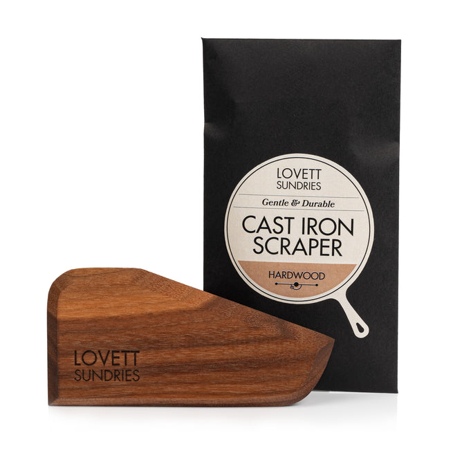 A handcrafted Lovett Sundries Cast Iron Scraper, featuring the brand’s engraving, is showcased in front of its black packaging labeled Lovett Sundries Cast Iron Scraper Hardwood.