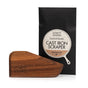 A handcrafted Lovett Sundries Cast Iron Scraper, featuring the brand’s engraving, is showcased in front of its black packaging labeled Lovett Sundries Cast Iron Scraper Hardwood.