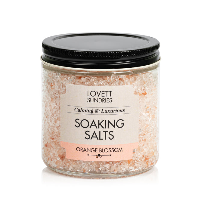 Lovett Sundries Soaking Salts come in a clear jar with a black lid. These pale pink, natural “Calming & Luxurious” salts in Orange Blossom scent are perfect for aromatherapy.