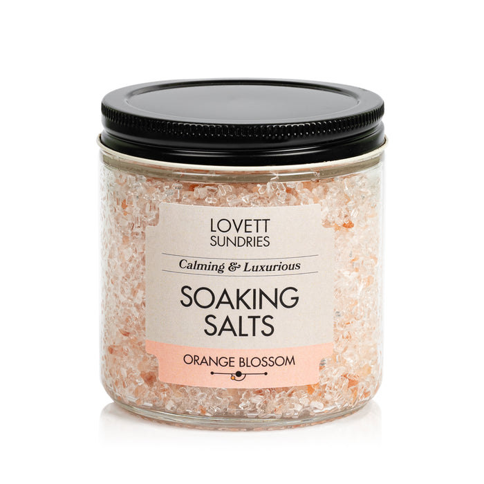 Lovett Sundries Soaking Salts come in a clear jar with a black lid. These pale pink, natural “Calming & Luxurious” salts in Orange Blossom scent are perfect for aromatherapy.