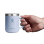 A hand holds a 12 oz light blue Hydro Flask Stainless Steel Mug with an insulated design and the brand logo on the front. The sleek style of this plain mug stands out against a white background.