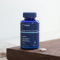 A blue Trace Minerals Magnesium Glycinate, 120mg bottle with 180 capsules rests on a wooden surface for sleep support, featuring bioavailable magnesium and two white capsules beside it.