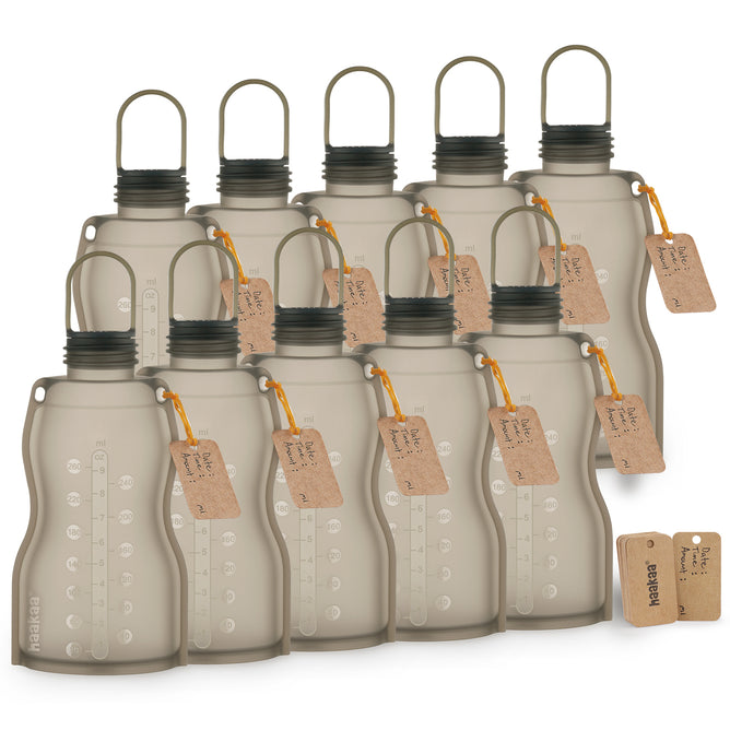 Ten beige Haakaa Reusable Breast Milk Storage Bags, made of 100% food-grade silicone with black caps and loop handles, are arranged in rows. Each freezer-safe bag has a brown tag with an orange string and visible measurement markings; two spare tags are nearby.