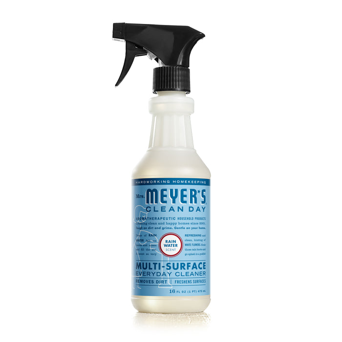 A white plastic spray bottle of Mrs. Meyer’s Clean Day Multi-Surface Everyday Cleaner, with a black spray nozzle and a blue label detailing product information, set against a white background.