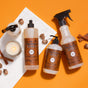 Mrs. Meyers Autumn Breeze Cleaning Set sits on a white marble tray with a lit candle, cinnamon sticks, and acorns against an orange background.