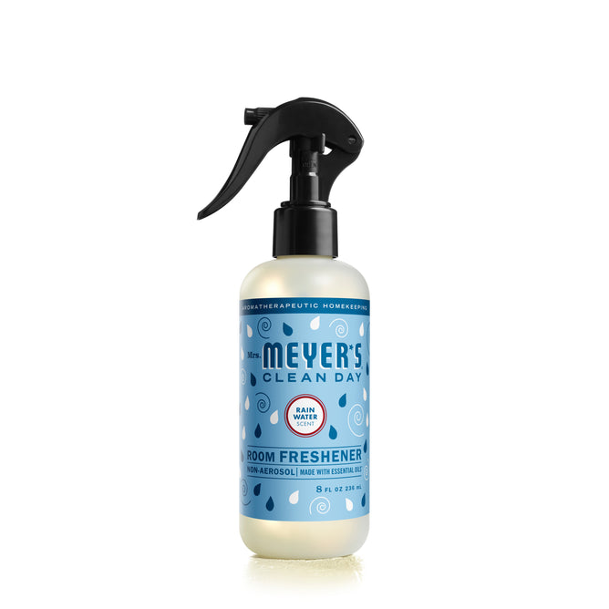 The Mrs. Meyers Room Freshener boasts a black spray nozzle and a blue label with raindrop designs, emphasizing its aromatherapeutic benefits with essential oils in a refreshing Rain Water scent.