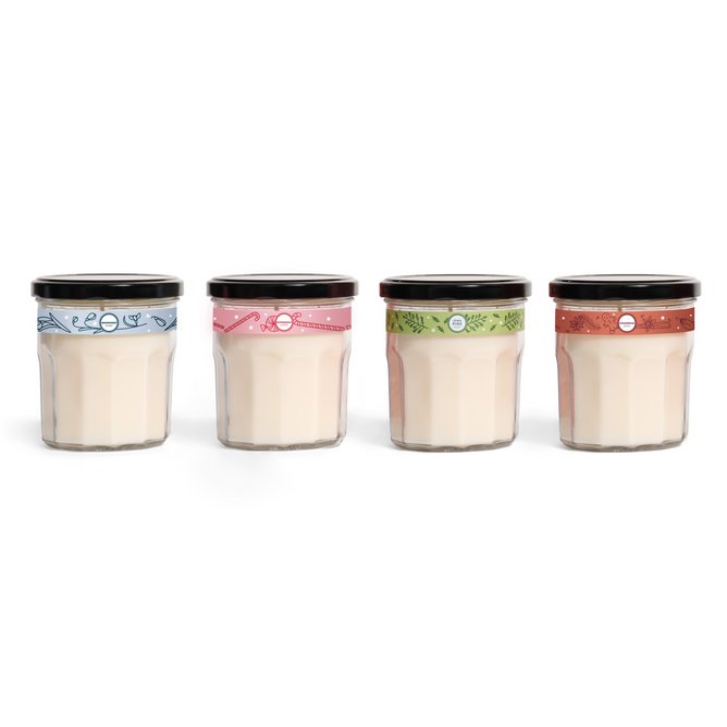The Mrs. Meyer's Holiday Glass Candle Collection features four glass jars with black lids and colored bands—blue, pink, green, and orange—each filled with a creamy candle.