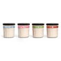 The Mrs. Meyer's Holiday Glass Candle Collection features four glass jars with black lids and colored bands—blue, pink, green, and orange—each filled with a creamy candle.