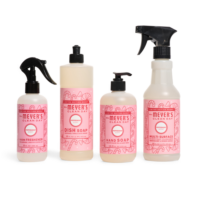 Four Mrs. Meyer’s “A Touch of Holiday Magic” cleaning products with pink peppermint labels are neatly arranged: a room freshener spray, dish soap, hand soap with pump, and multi-surface spray bottle.