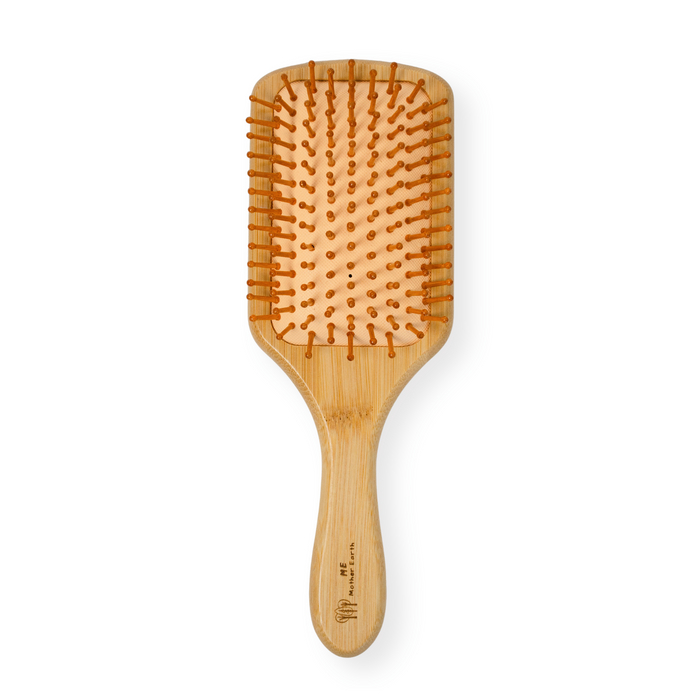 The Me Mother Earth Bamboo Paddle Hairbrush features a light wood handle, orange-tipped bristles on a natural rubber cushion, and a rectangular base—perfect for smooth, detangled hair. Shown against a white background.
