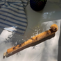 The Me Mother Earth Coconut Bottle Cleaning Brush with coconut husk bristles rests on a white surface, casting a shadow. Nearby are a blue-and-white striped cloth and a dark vase, creating an eco-friendly cleaning scene.