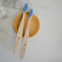 Two Me Mother Earth Kids Colorful Bamboo Toothbrushes with castor oil bristles rest on a round wooden dish atop white marble—an elegant, eco-friendly choice for sustainable oral care.