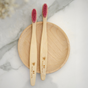 Two Kids Colorful Bamboo Toothbrushes with castor oil bristles by Me Mother Earth rest on a round wooden tray atop white and gray marble—a stylish, sustainable choice for children’s oral care.