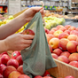 A shopper places a red apple into a Me Mother Earth Cotton Mesh Produce Bag (3 Pack) while selecting fresh produce in the grocery store’s fruit section.