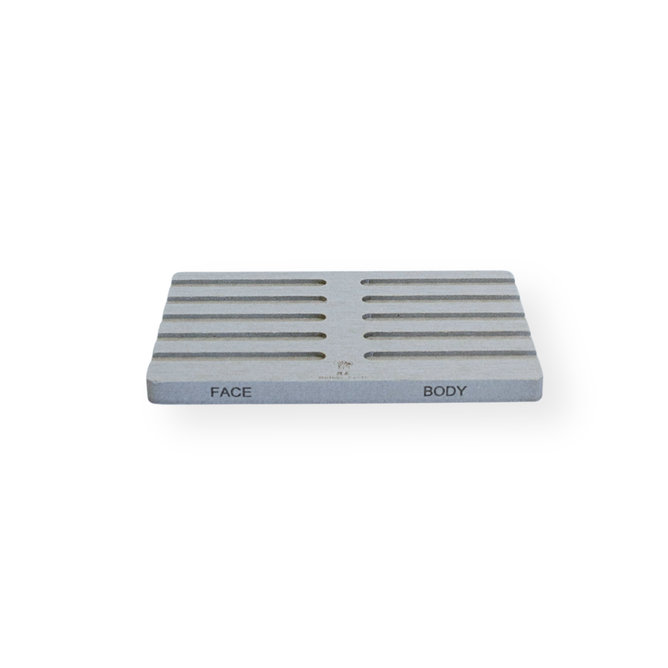 The Me Mother Earth Quick-Dry Diatomite Soap Dish, Face + Body, is a rectangular, light gray tray with horizontal grooves and FACE/BODY labels for quick-drying convenience, shown on a white background.