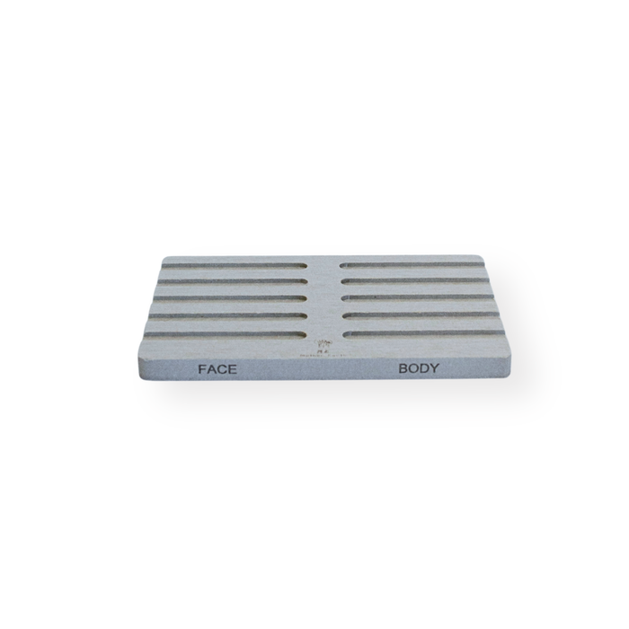 The Me Mother Earth Quick-Dry Diatomite Soap Dish, Face + Body, is a rectangular, light gray tray with horizontal grooves and FACE/BODY labels for quick-drying convenience, shown on a white background.